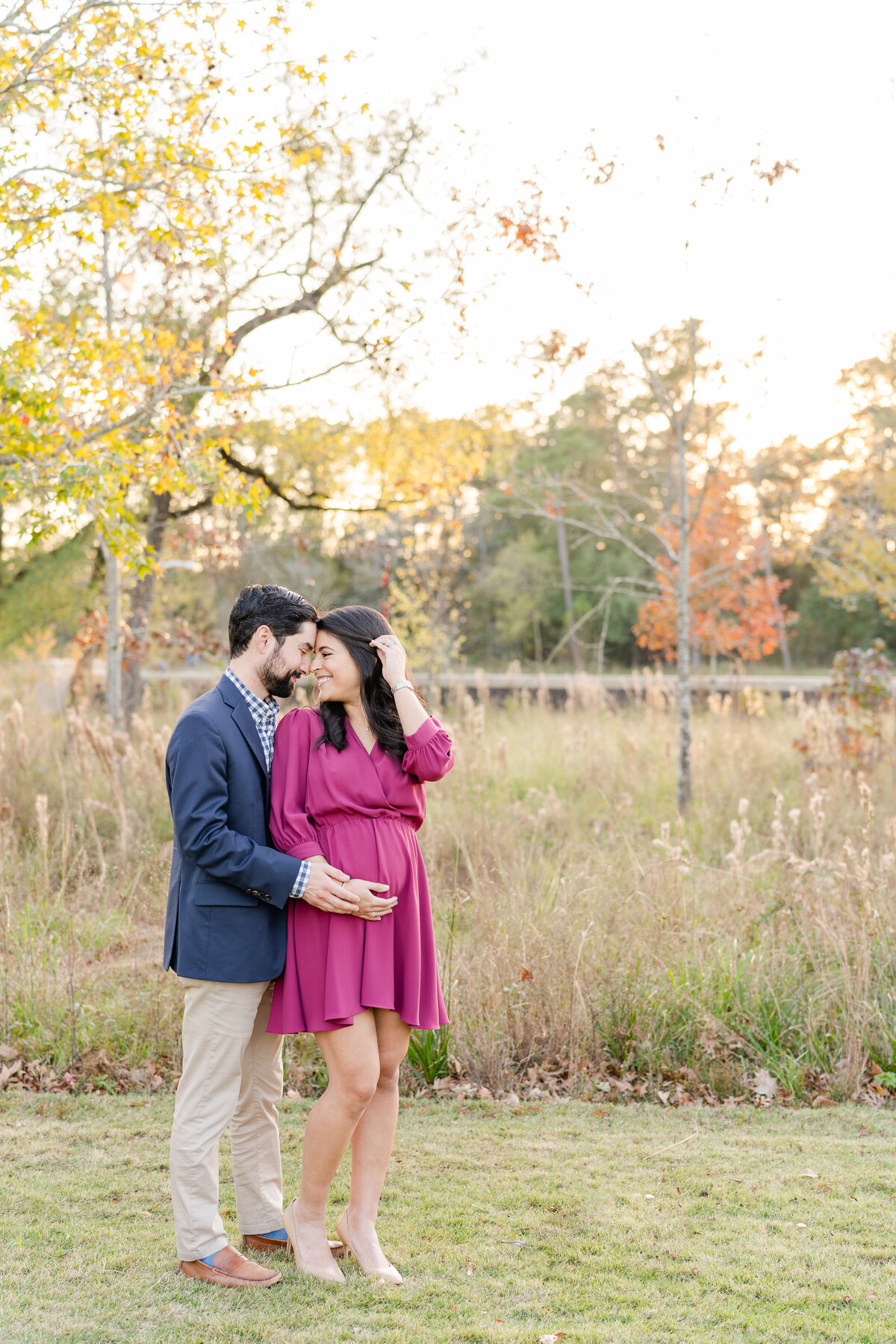 Husband and wife foreheads touching smiling and holding pregnant belly at Memorial Park