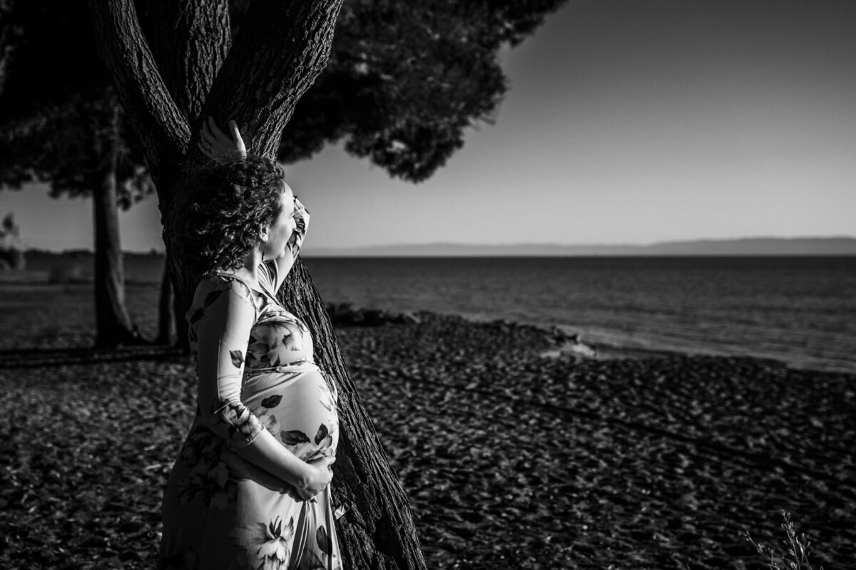 profile of pregnant woman leaning against a tree at the beach and looking out towards the ocean