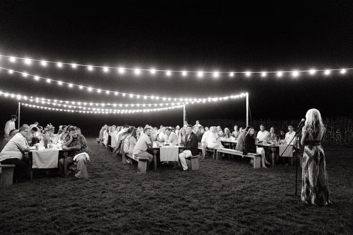 A girl is speaking in front of the guests at a dinner outdoors, adorned with fairy lights, at Lion Rock Farms, CT. Image by Jenny Fu Studio