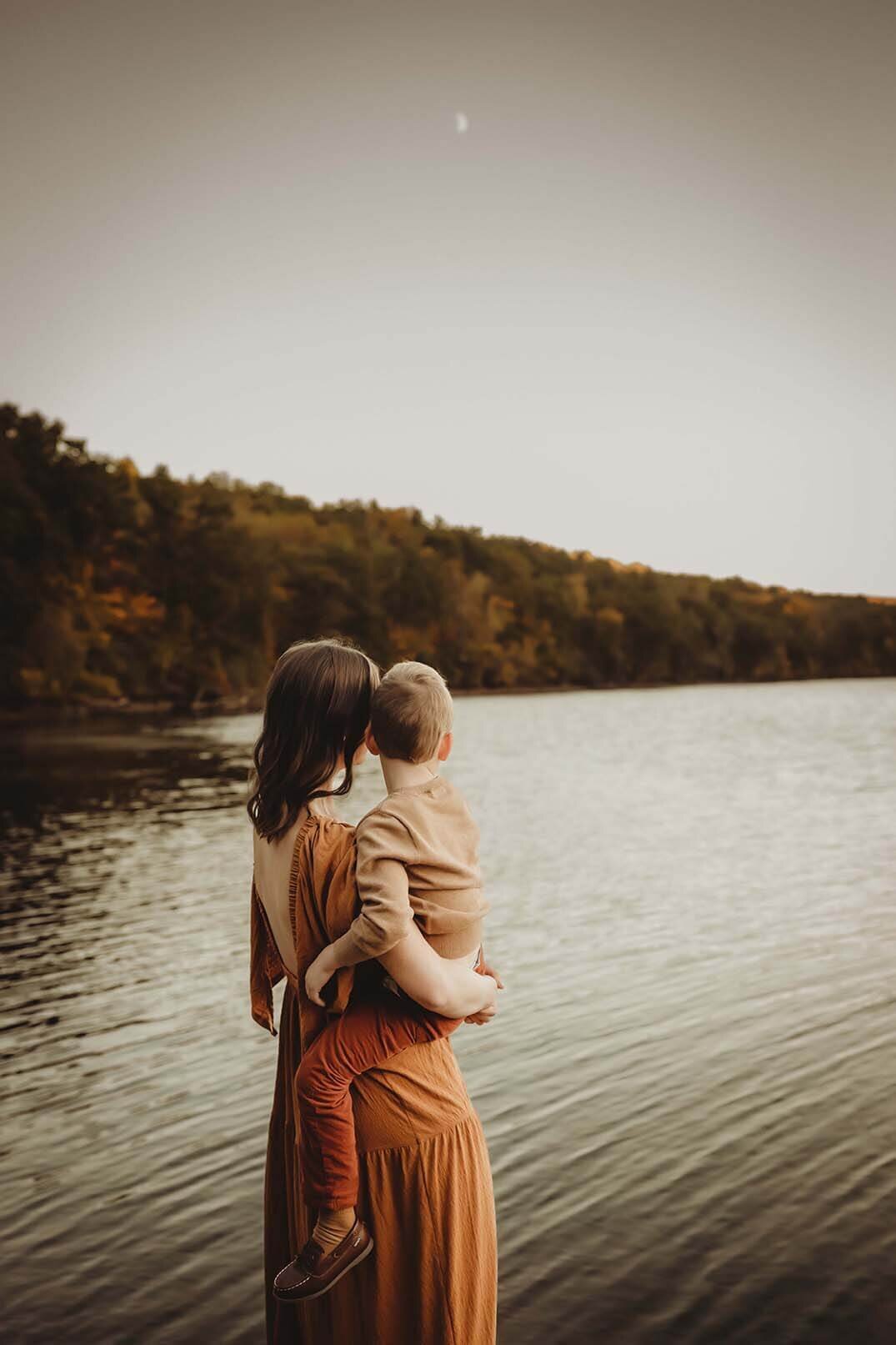 A mother and sun are sharing a quiet moment looking out at the lake with a crescent moon shining in the sky