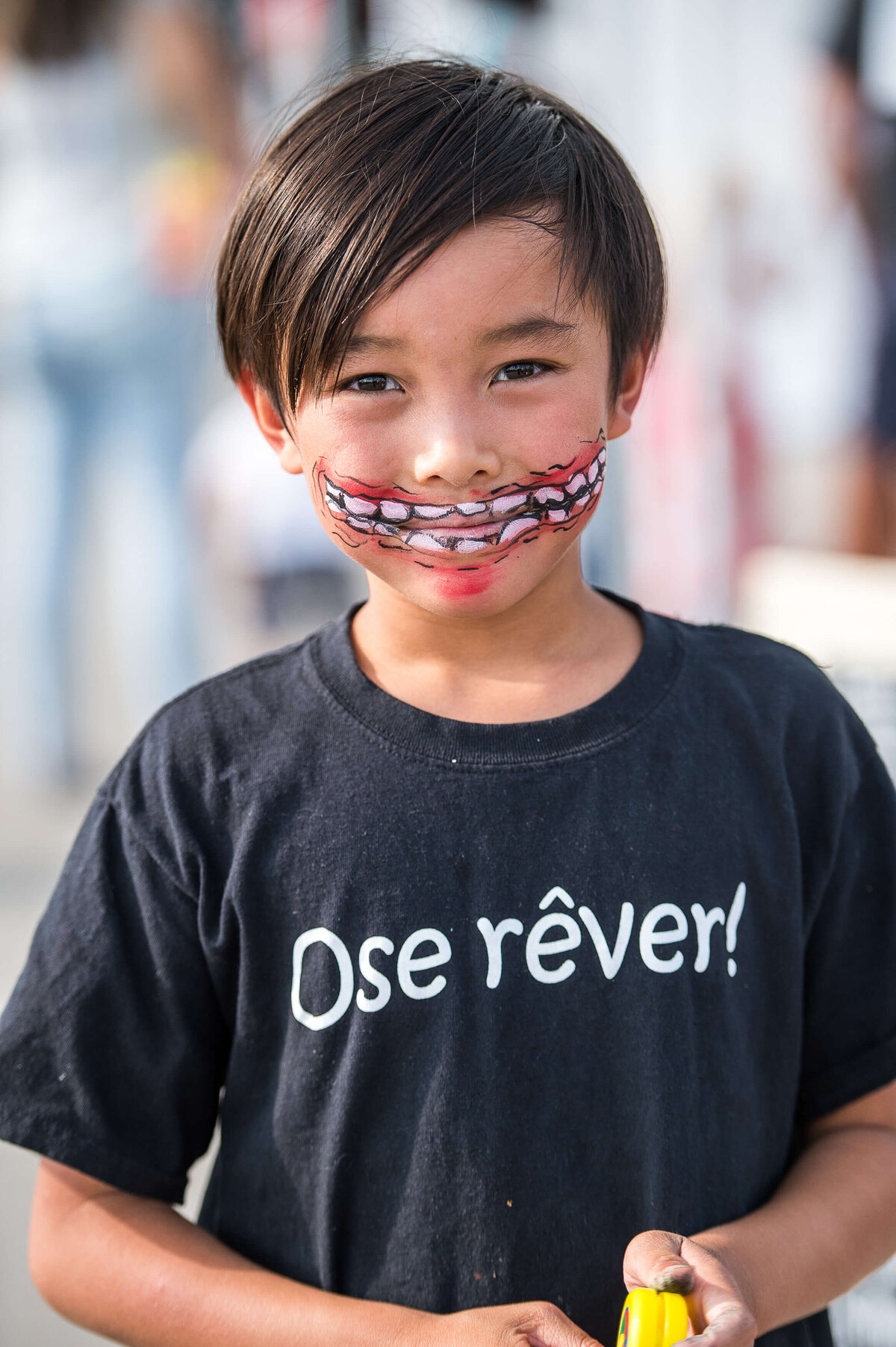 a portrait of a smiling boy in a black t-shirt with face makeup showing a wide grin.  Captured by Ottawa Event Photographer JEMMAN Photography COMMERCIAL during a corporate children's event