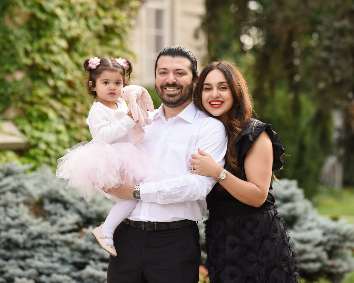 Dad holding young daughter with wife hugging dad family portrait in park