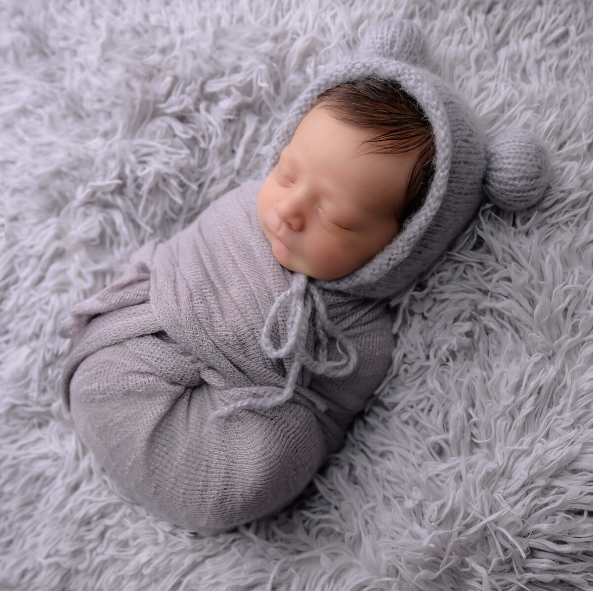 Kitsap Peninsula photographer Beth Benecki photographed a newborn wrapped in light gray with a gray bear bonnet sleeping peacefully on a fur blanket