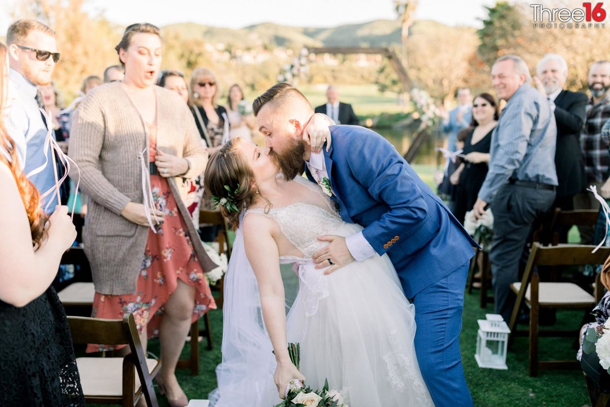 Groom dips his Bride to kiss her while walking up the aisle