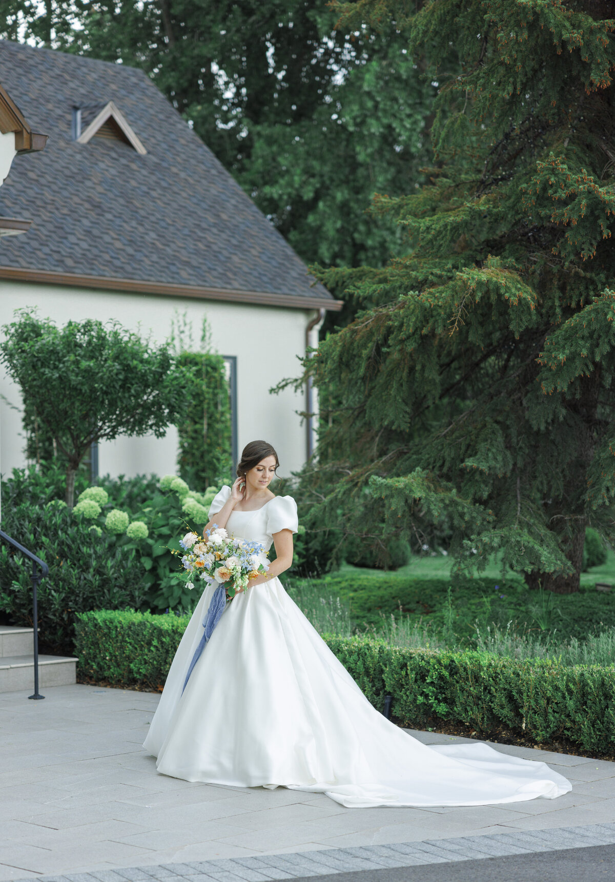 Bridal portrait, the bride in a long classic satin gown with puff sleeves, and a pastel bridal bouquet