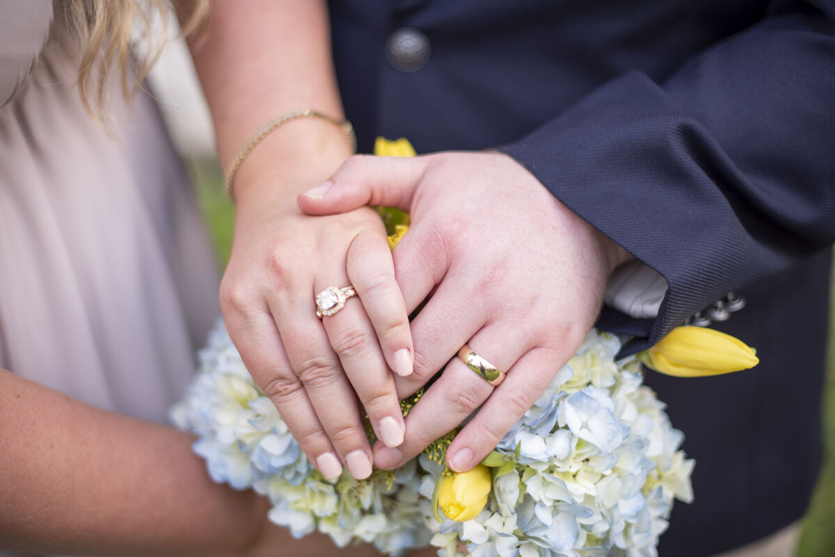 wedding rings on hands on top of bouquet