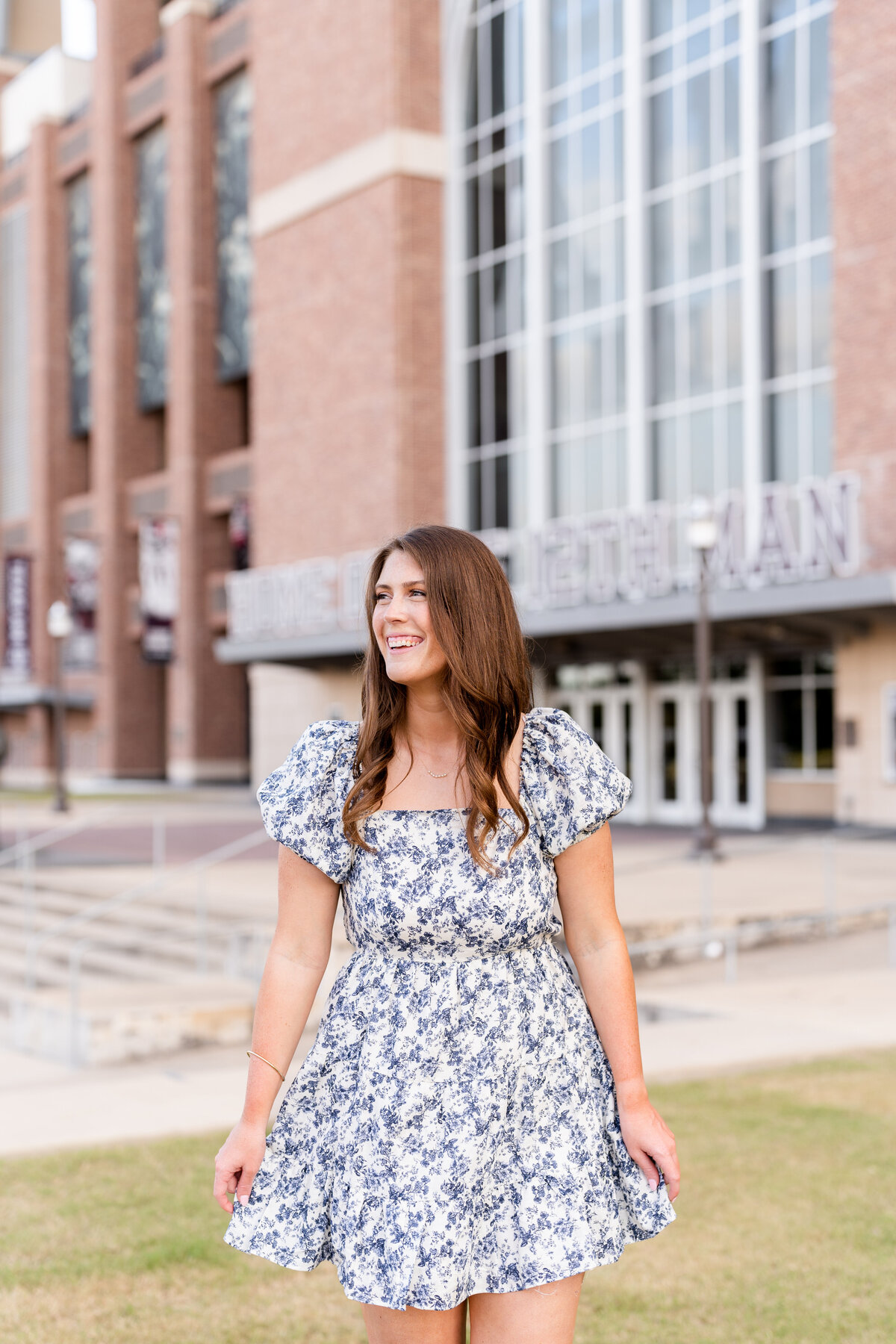 Texas A&M senior girl swishing dress and laughing over shoulder while walking and wearing blue and white dress in front of Kyle Field