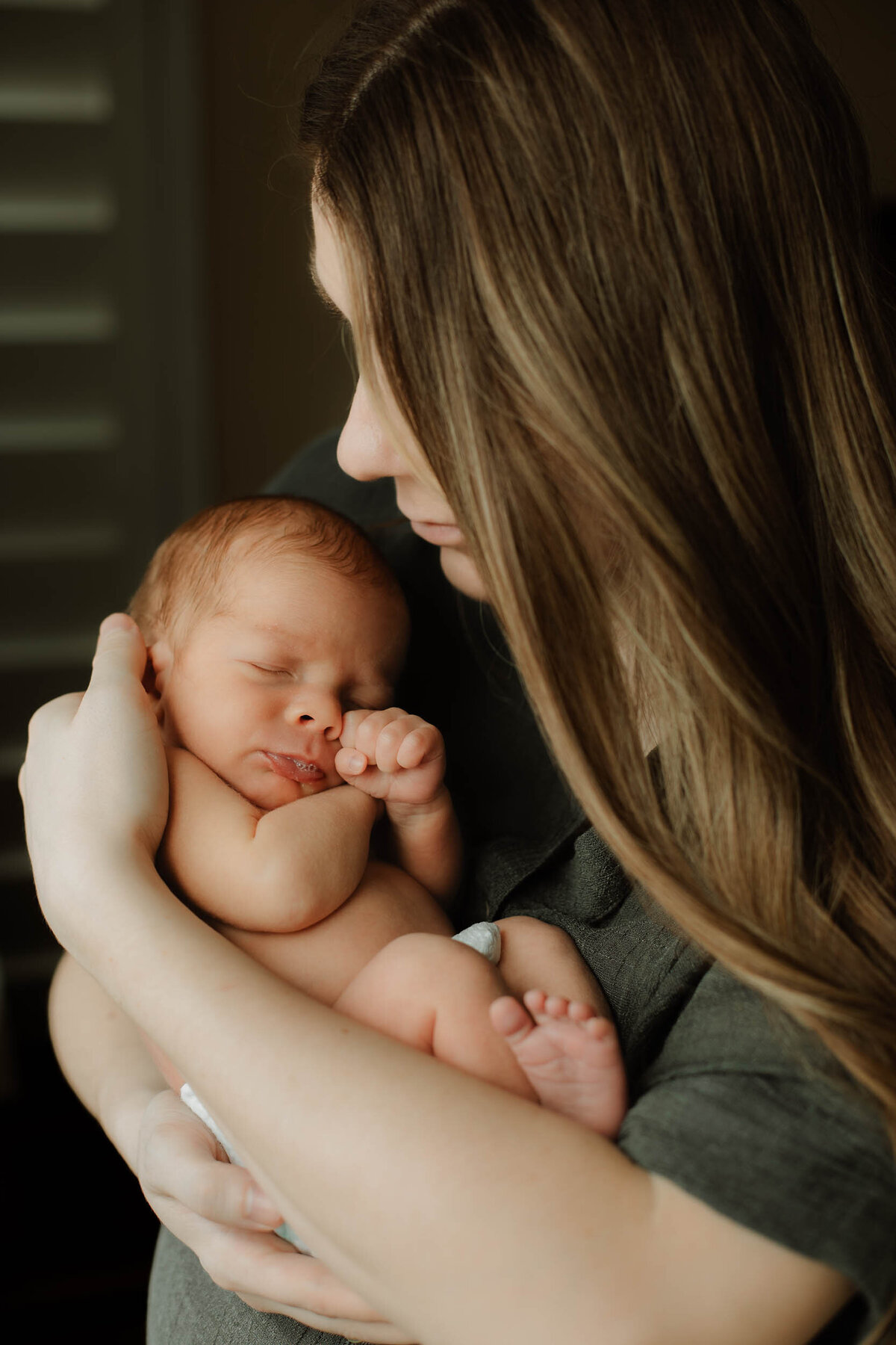 Mom cradling her newborn son in her arms while in diaper only during an at-home newborn session.