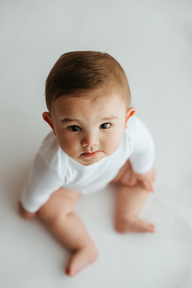 six month old in tight white onesie while sitting straight up