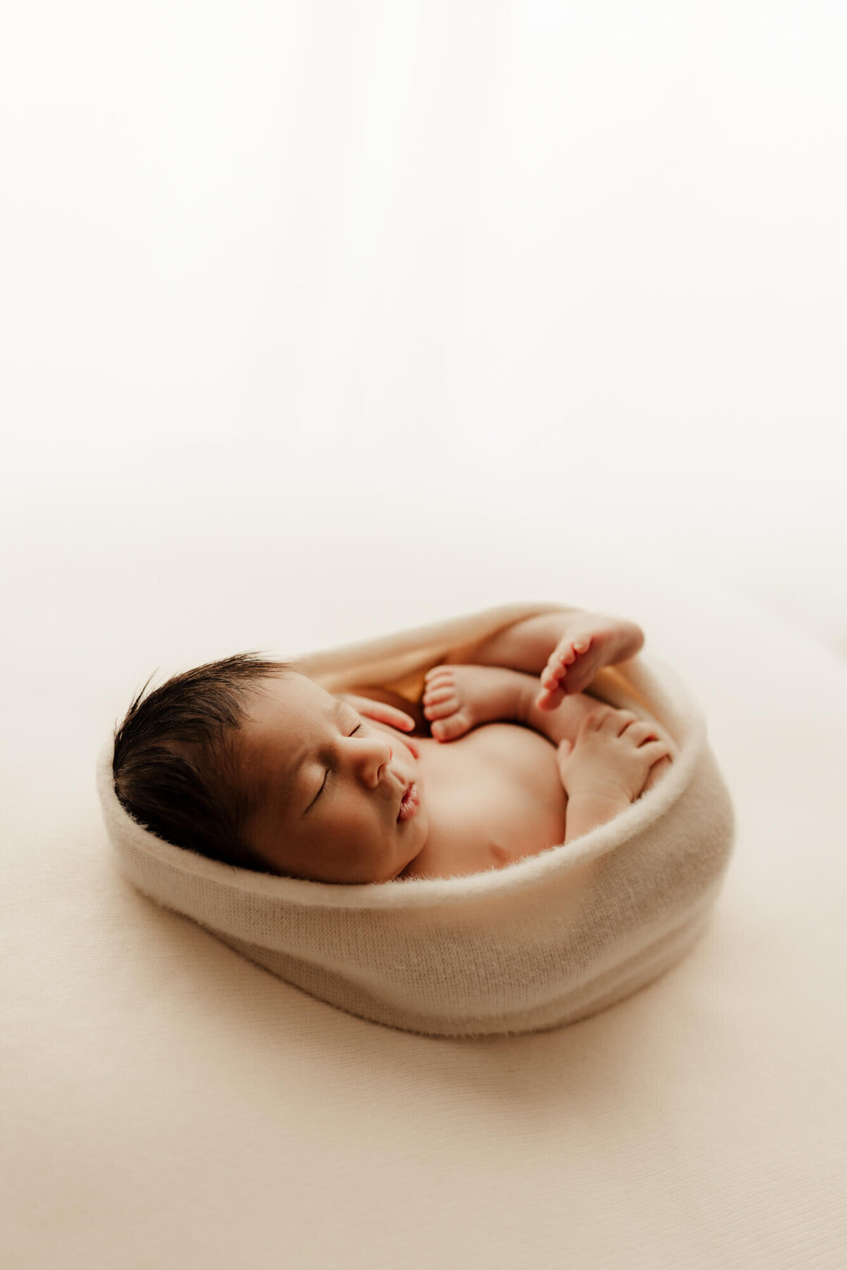 Newborn baby boy swaddled in a cream colored wrap for a newborn photo in OKC.