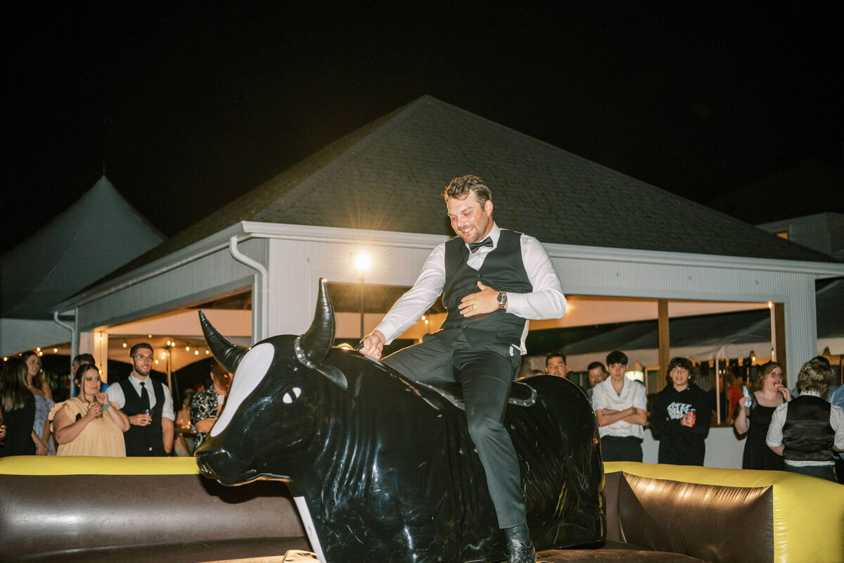 A groom rides a mechanical bull at his outdoor Oregon wedding reception.