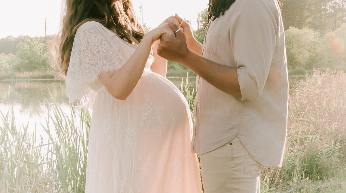 close up of a pregnant woman and man holding hands by a lake in raleigh