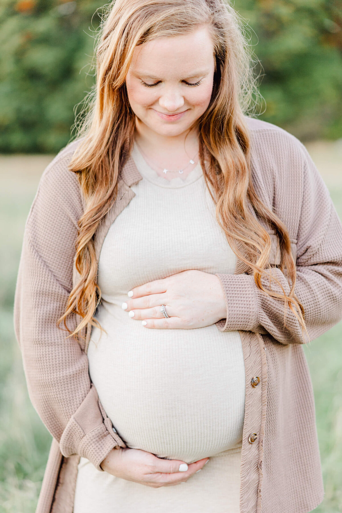 A mom cradles her baby bump and smiles in a meadow