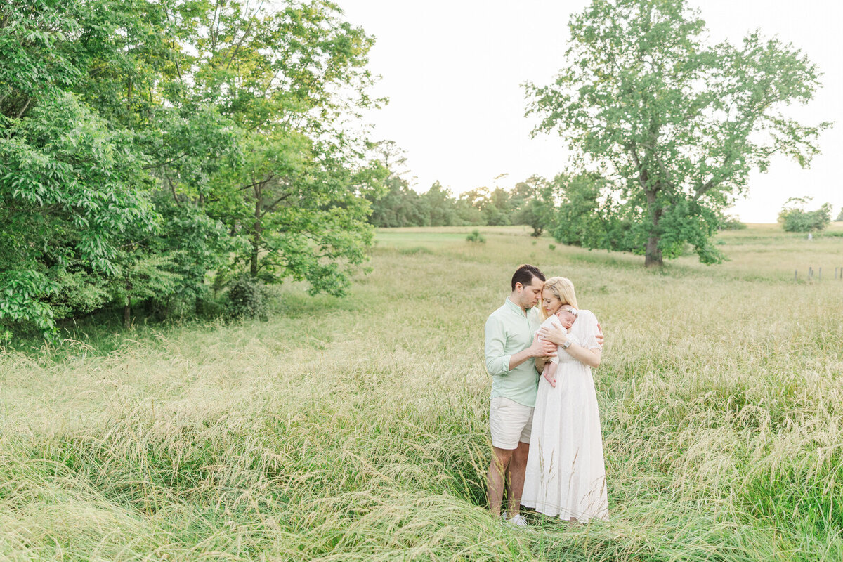 Mom and dad stand in tall grass snuggling newborn baby in Dacula, Georgia