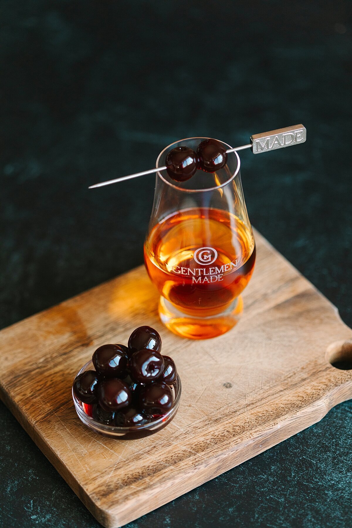 Bourbon cocktail product photography with dark cherries and a cocktail pick in Carlsbad, California.