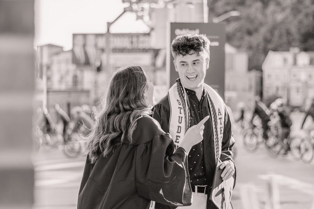 College graduate couple laughing during candid moment at senior photo session in Pittsburgh outside of Carlow University.