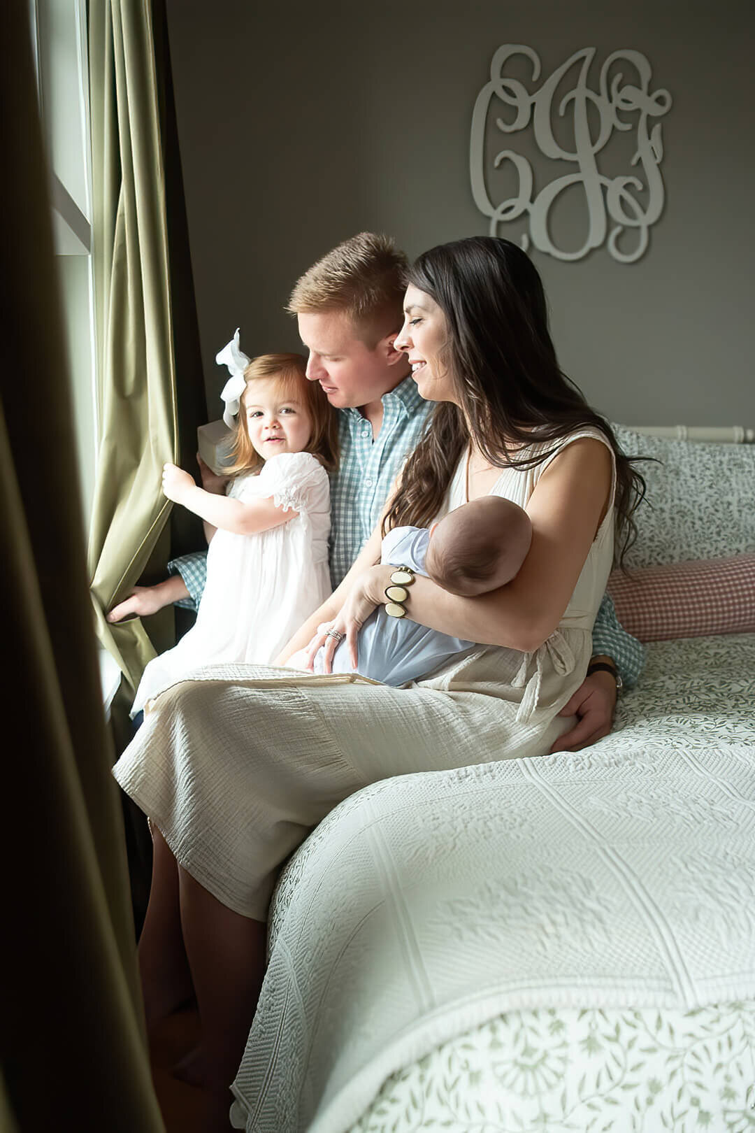 A young family looks out the window of their Salem home as their newborn sleeps in the mom's arms.