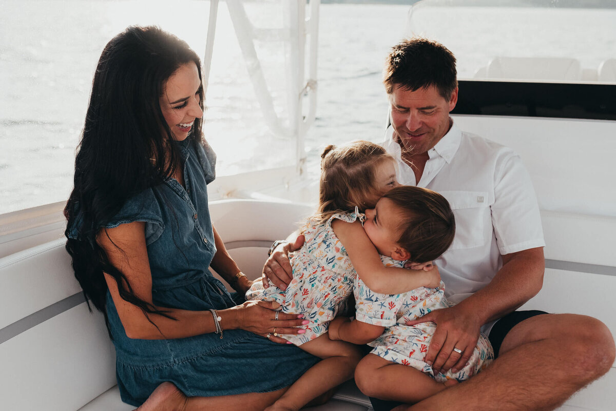 A mother and father and their young son and daughter snuggle together on their boat at sunset