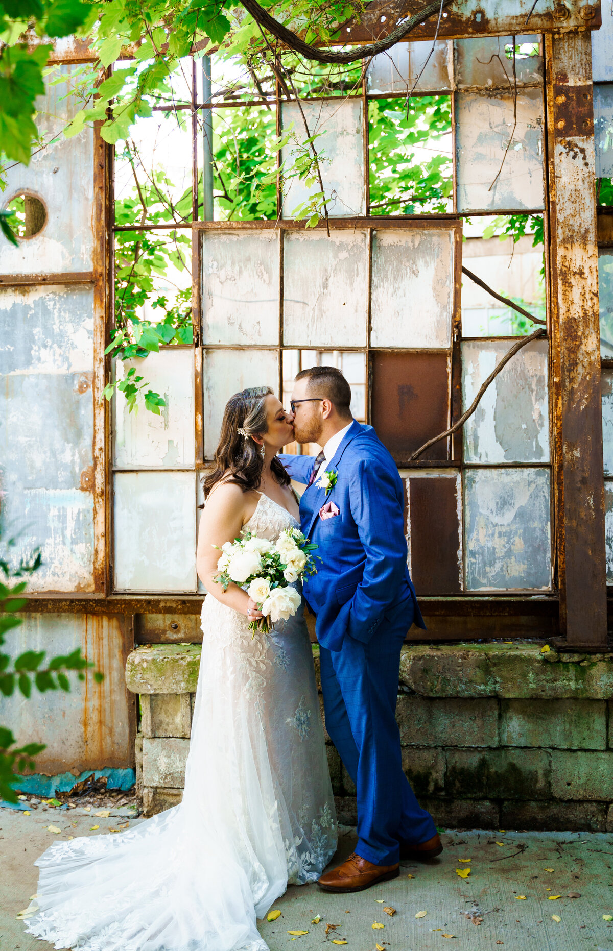 Bride and groom sharing a kiss in front of some old industrial windows at Strongwater Events in Columbus, Ohio.