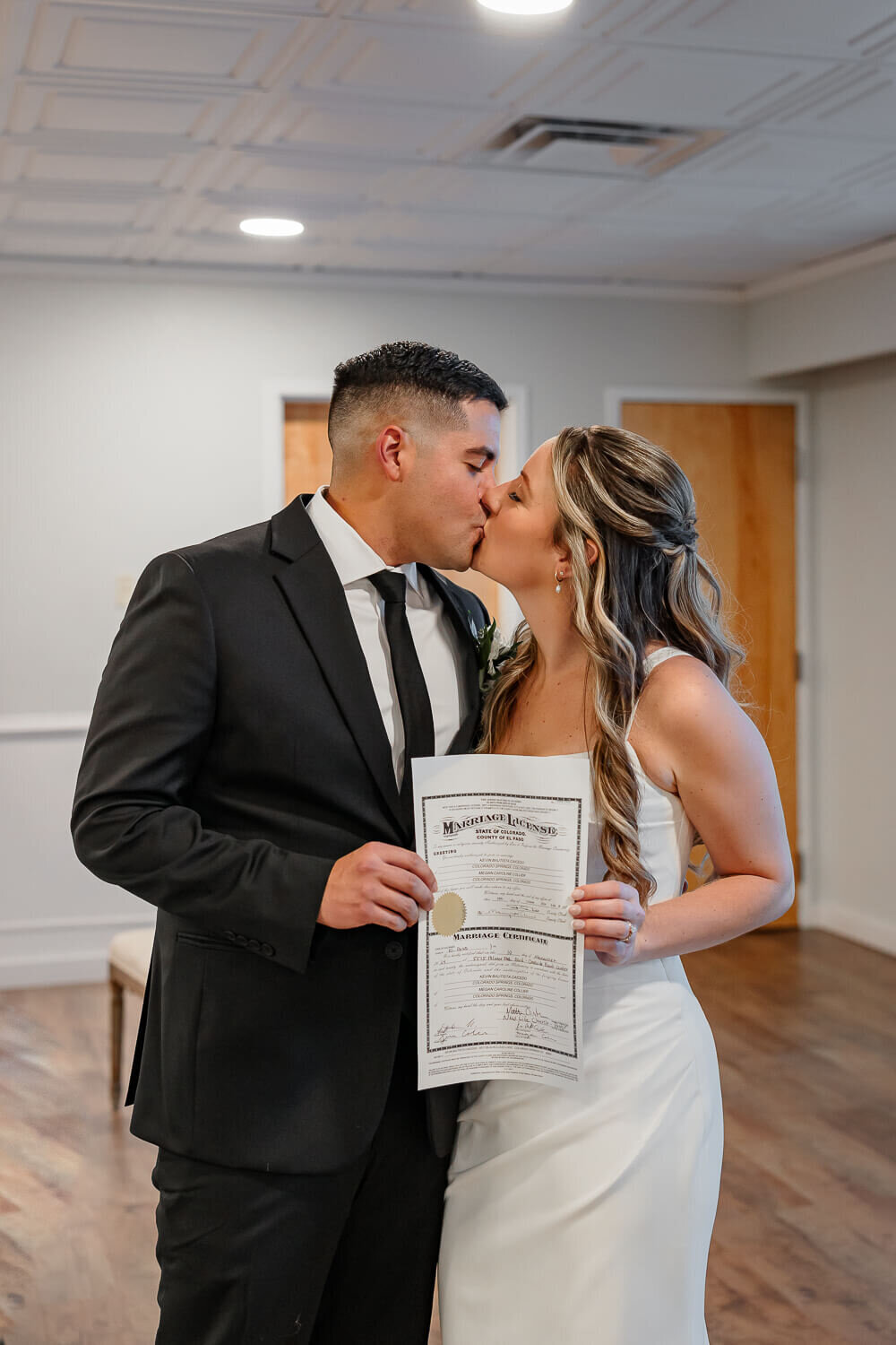 Smiling bride and groom embracing while kissing holding the wedding contract, captured by Colorado Springs wedding photographer, Michelle Betz Photography