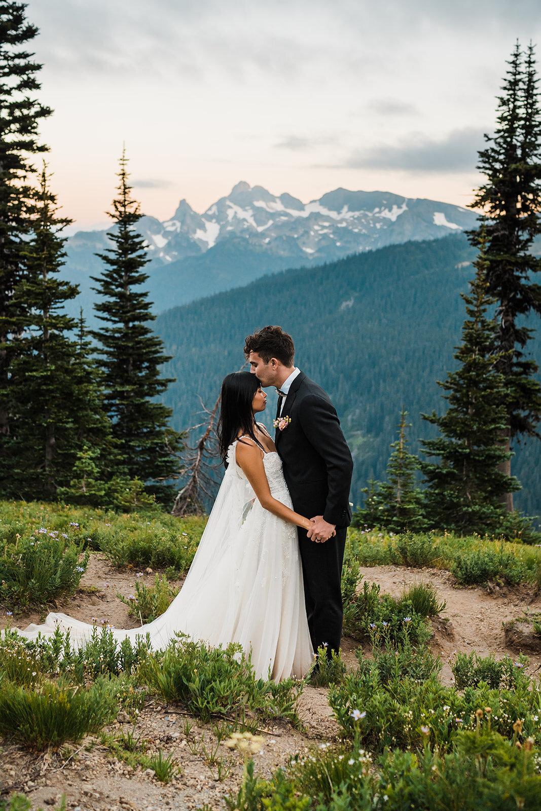 Groom kissing brides forehead and holding her hand along trail in Mount Rainier National Park after their elopement ceremony!