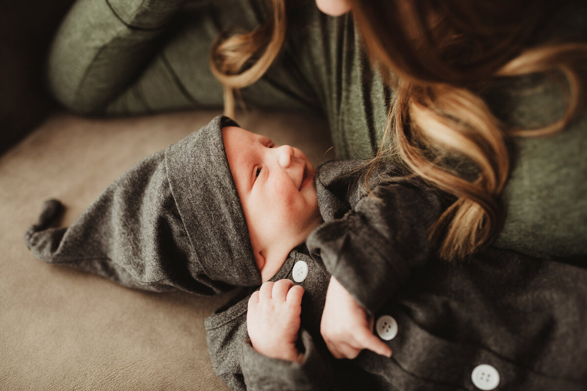 Newborn son wearing charcoal gray romper smiling at his mom.