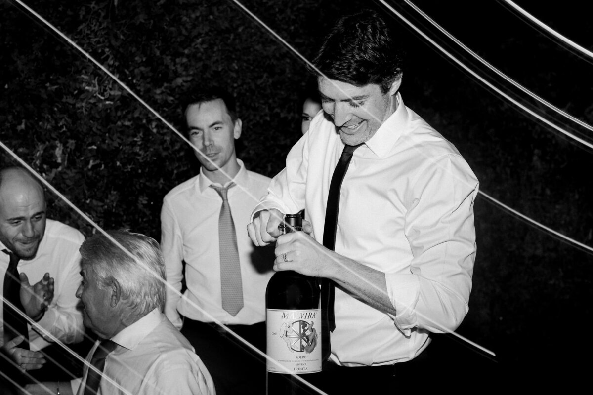 man opening large wine bottle smiling at italian wedding reception black and white