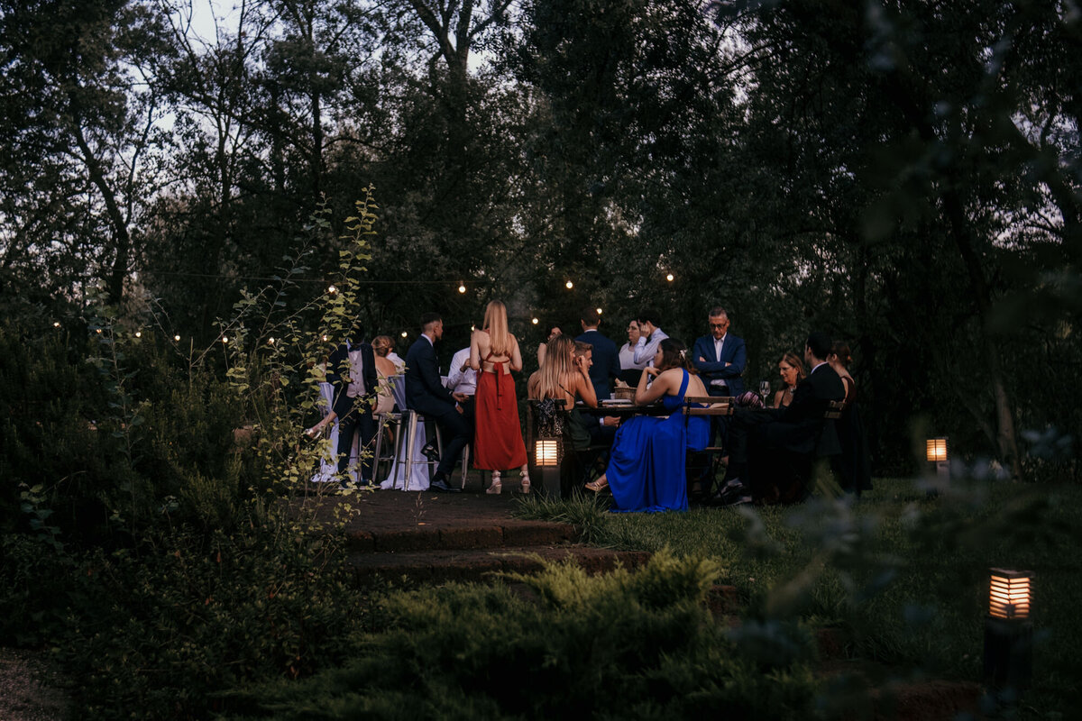 The wedding guests celebrate outside at a garden flair venue with fairy lights.