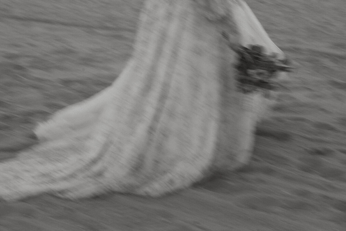 A slightly blurred photo of someone in a wedding dress walking on the beach