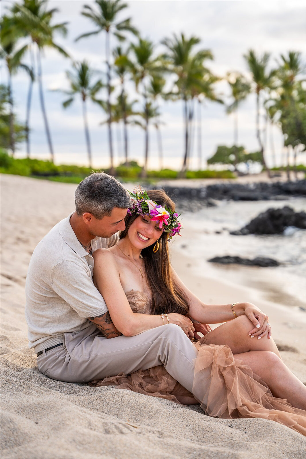 Couple sitting on the beach embracing for Hawaii engagement photos