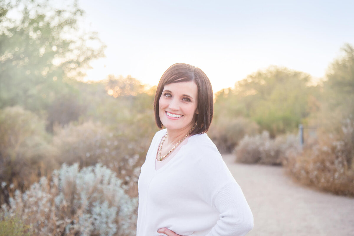 Pretty woman with short brown hair in white shirt smiling on a desert path