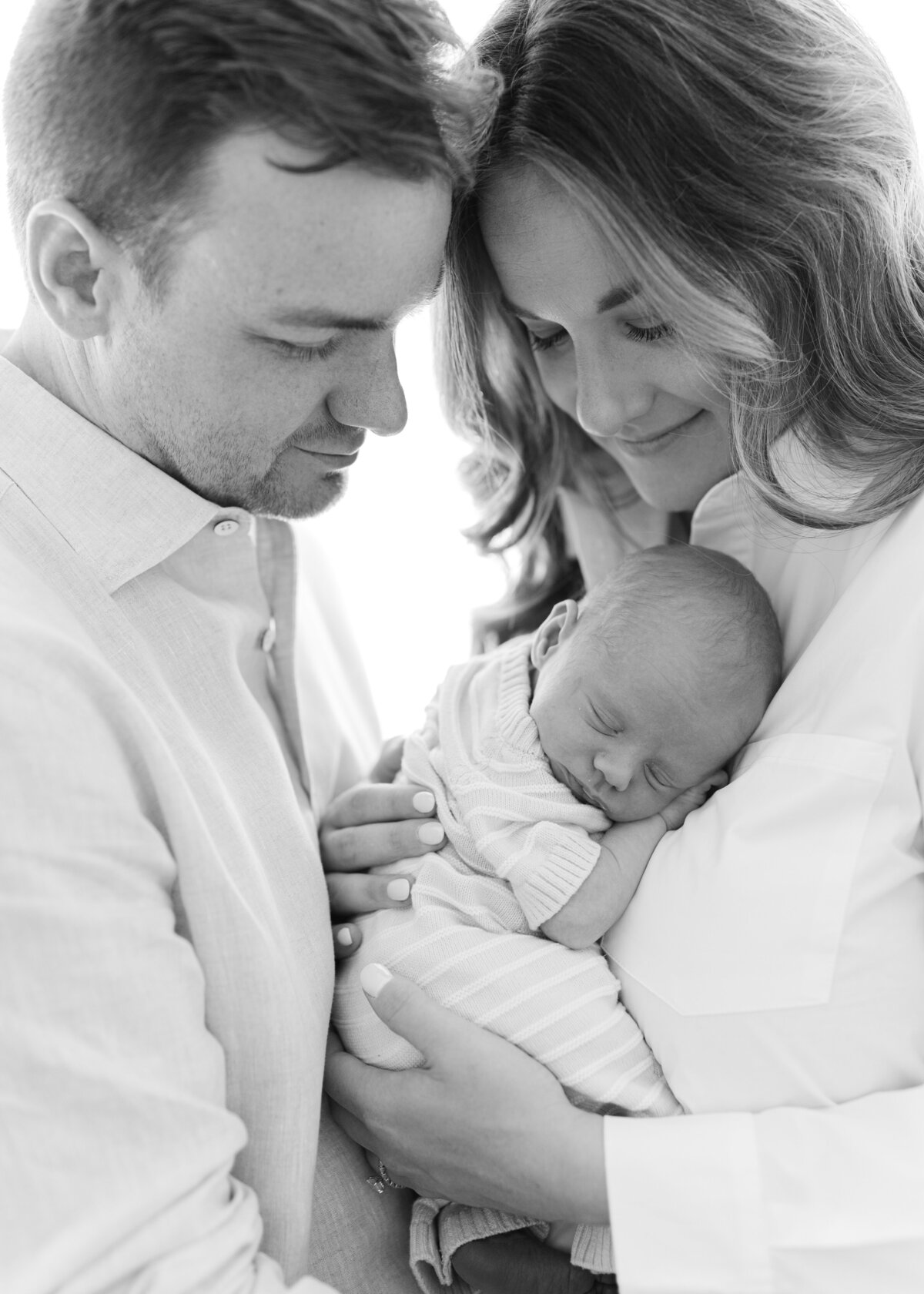 Bland and white image of a baby snuggling on his mother's chest and the mom and dad are smiling looking down at the baby. Photo by Denver photographer Maegan R Photography