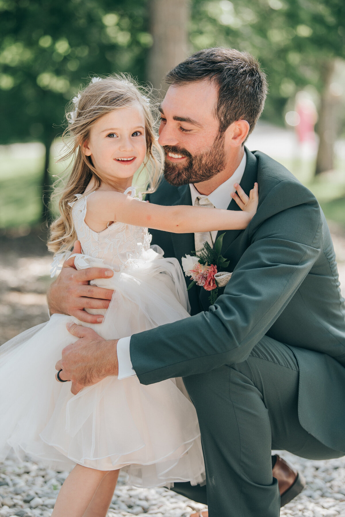 Groom wearing a green suit posing with his daughter, the flower girl on a Summer wedding day