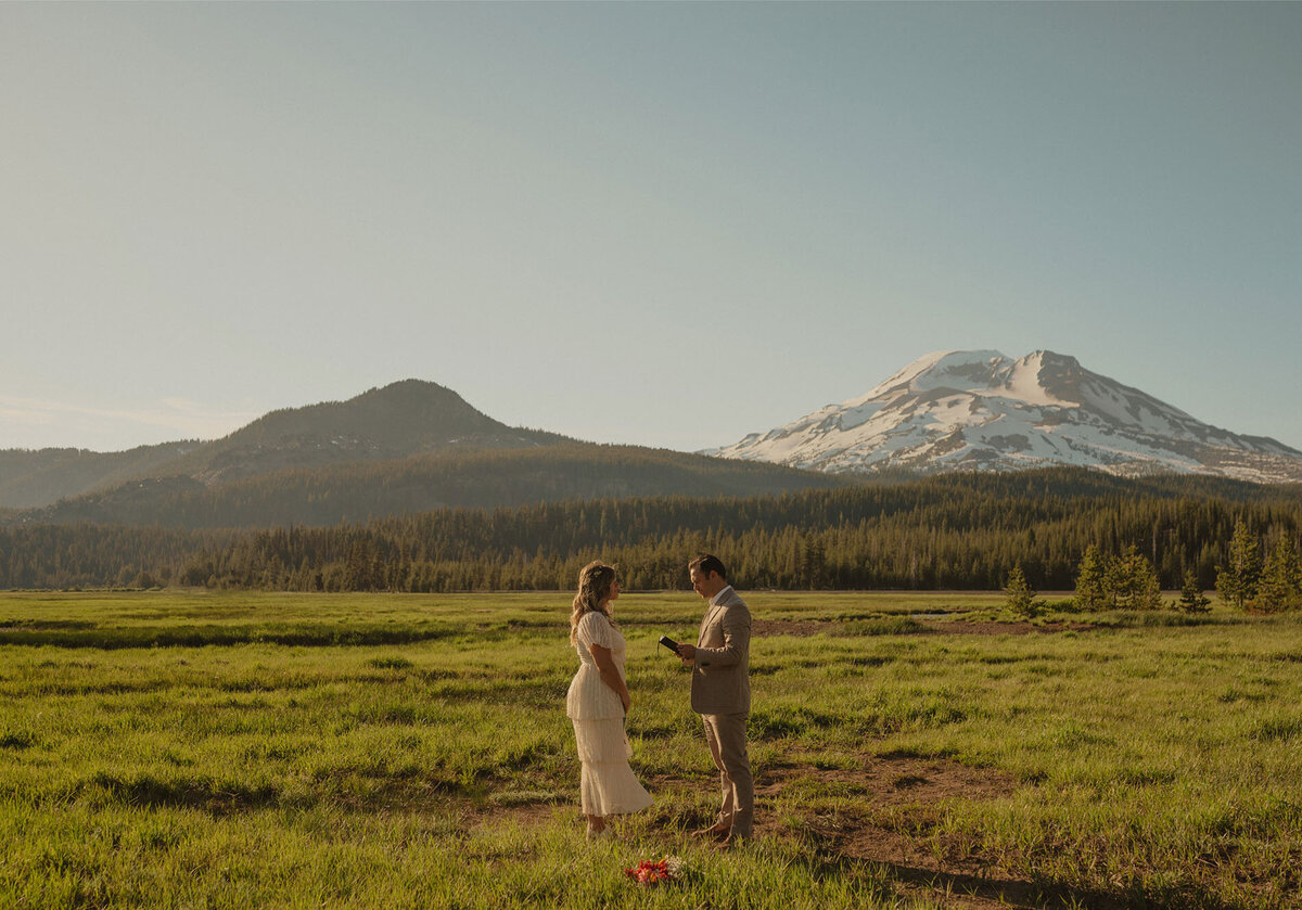 bride and groom exchange vows amongst an open green meadow in front of Mt. Bachelor in central Oregon
