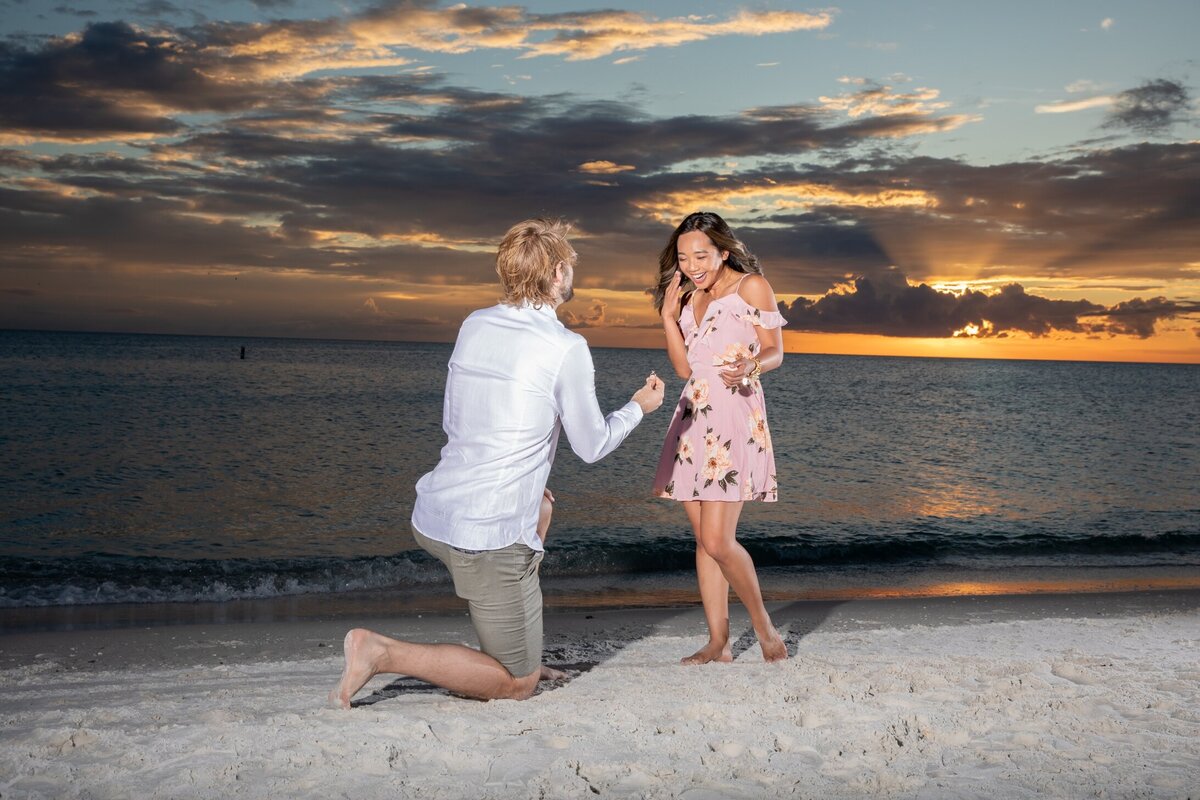 A man on one knee holding a ring and proposing to his girlfriend at Bradenton Beach, Fl at sunset.