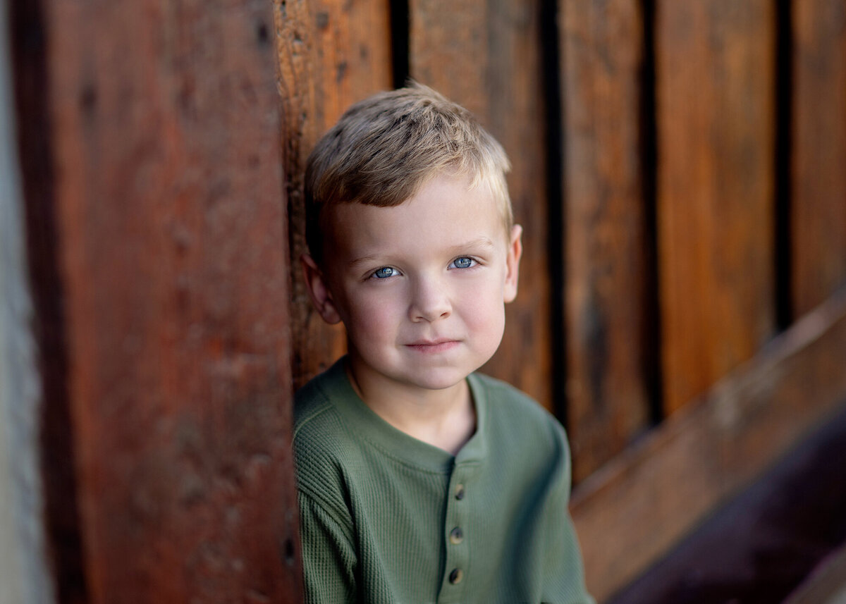 A child stands alone against a dark wooden wall, their gaze intense
