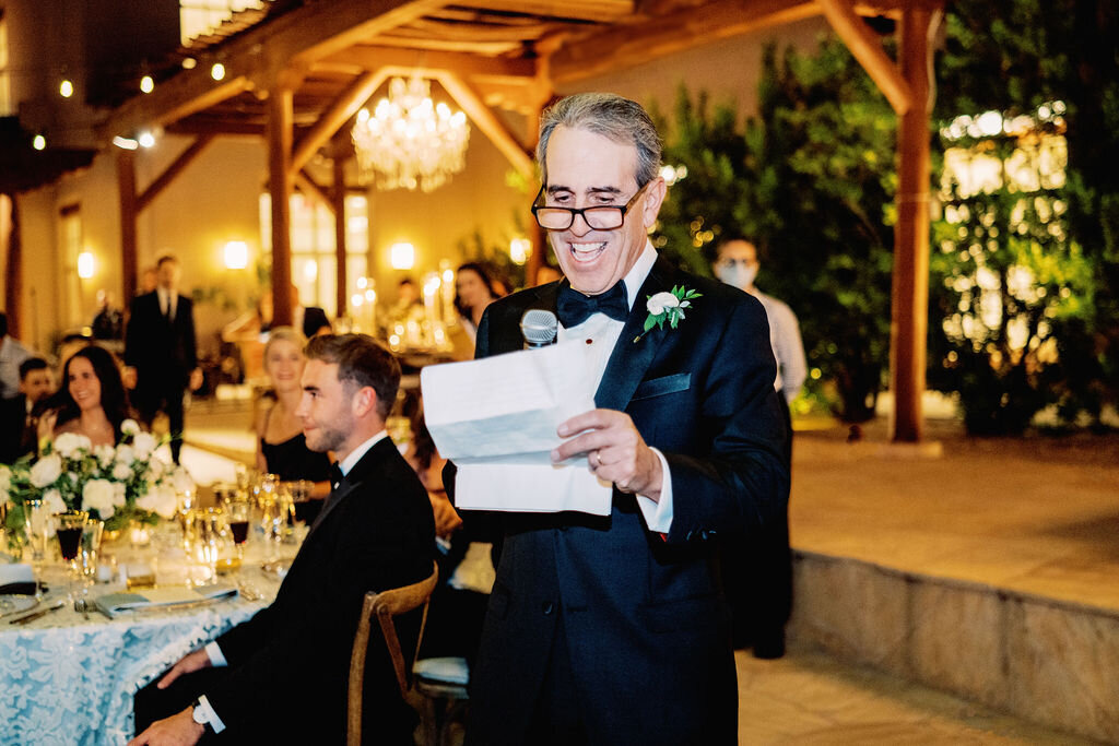 The father of the groom delivers an emotional and heartfelt wedding toast, surrounded by elegant candlelit decor and joyful guests.
