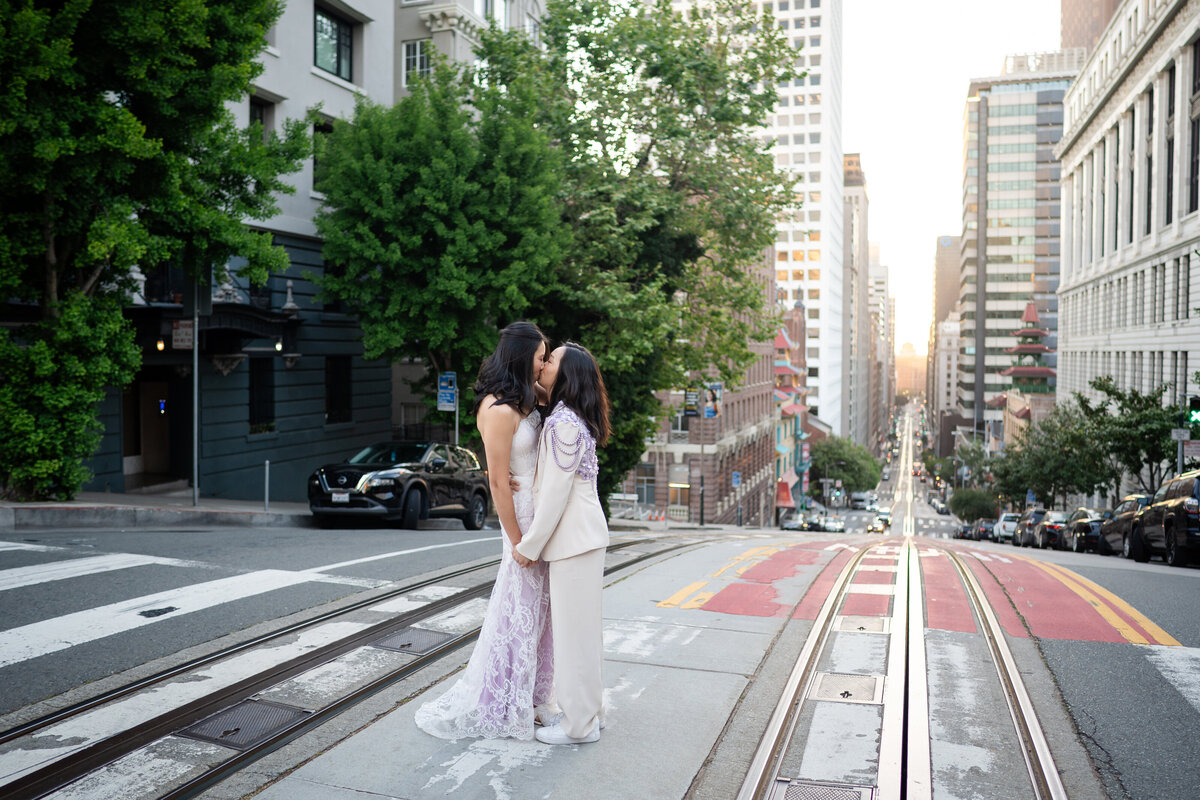 Queer lesbian couple in San Francisco during sunrise in the middle of the street kissing each other with the Golden State Bridge in the background
