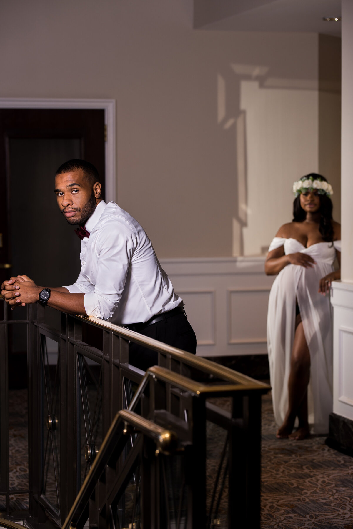 a Black couple lean against a railing and wall, looking into the camera