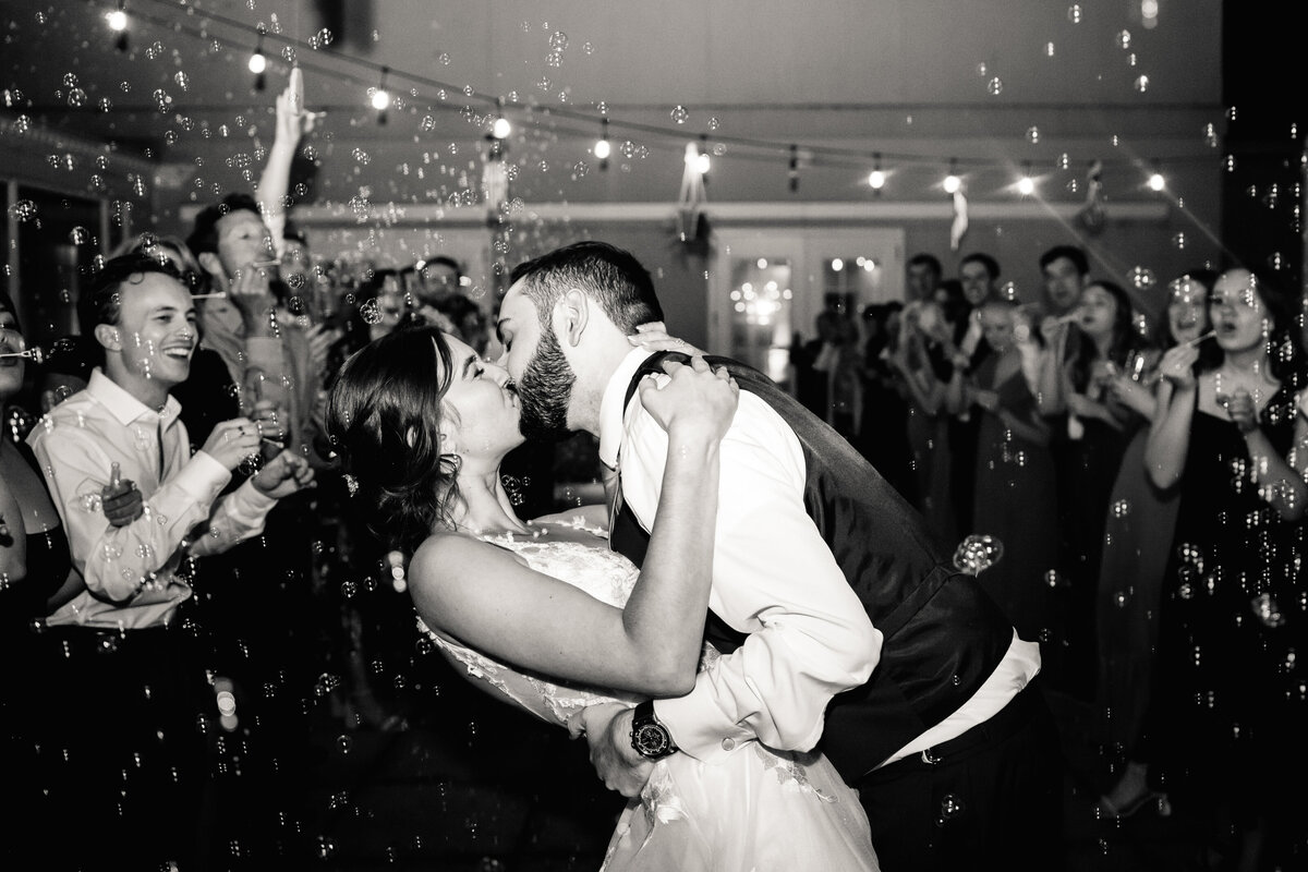 A newlywed couple kissing with guests cheering in the background