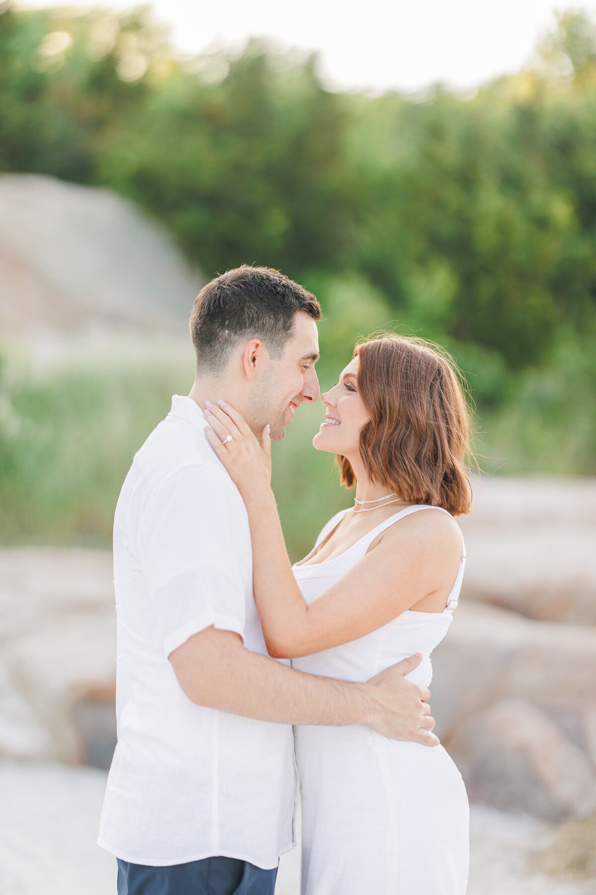 A woman lovingly holding her fiance's face during their Wingaersheek Beach engagement pictures