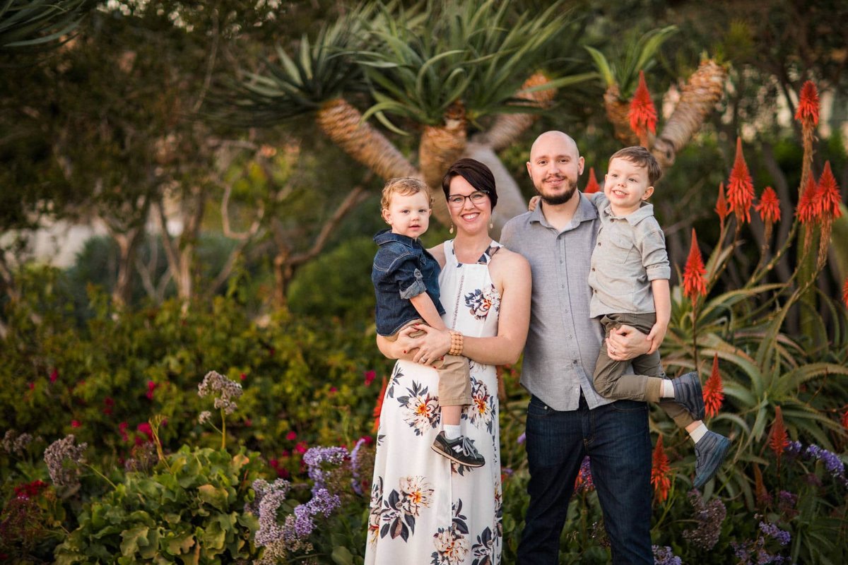 Parents hold their two young boys as they pose for a family photo with tropical plants behind them