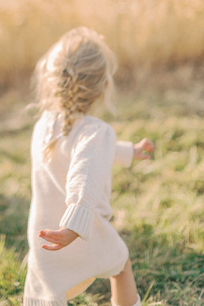 Girl with white sweater dress and braid running in a field