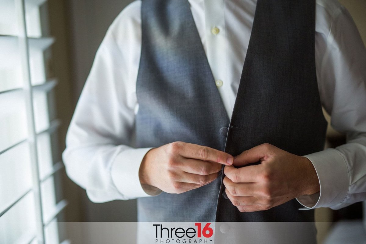 Groom buttoning his vest before the ceremony