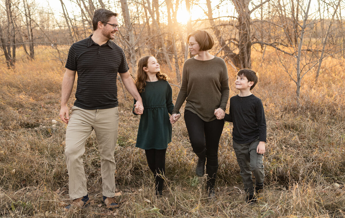 family smiling holding hands in forest during sunset