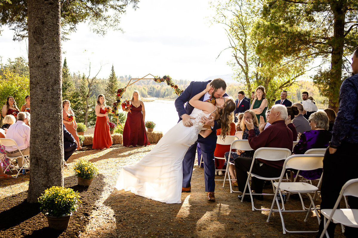 groom dipping and kissing his bride after wedding ceremony as bridesmaids look on.