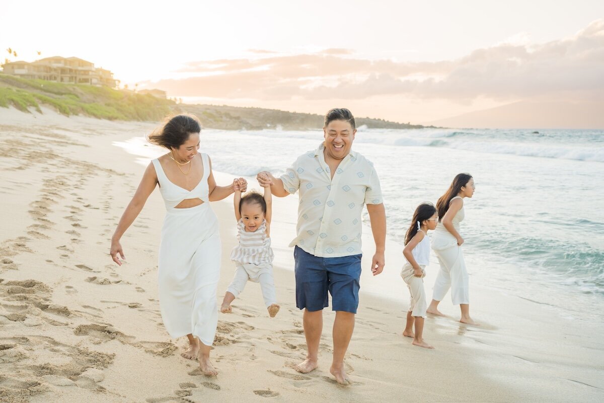 Family of five playing on the beach in Maui, swinging little boy and girls playing in the water.