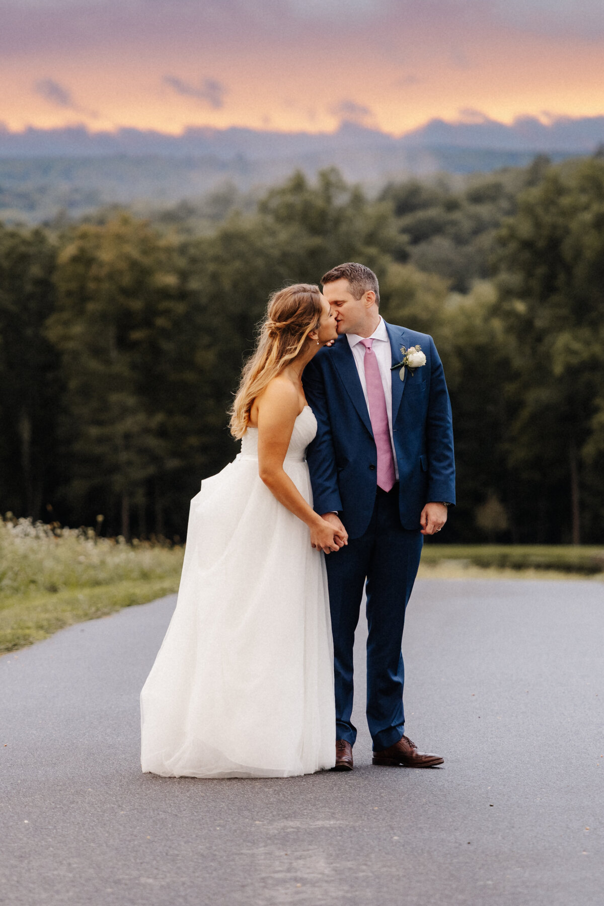 Romantic sunset wedding portrait of a bride and groom kissing with mountain views behind them.