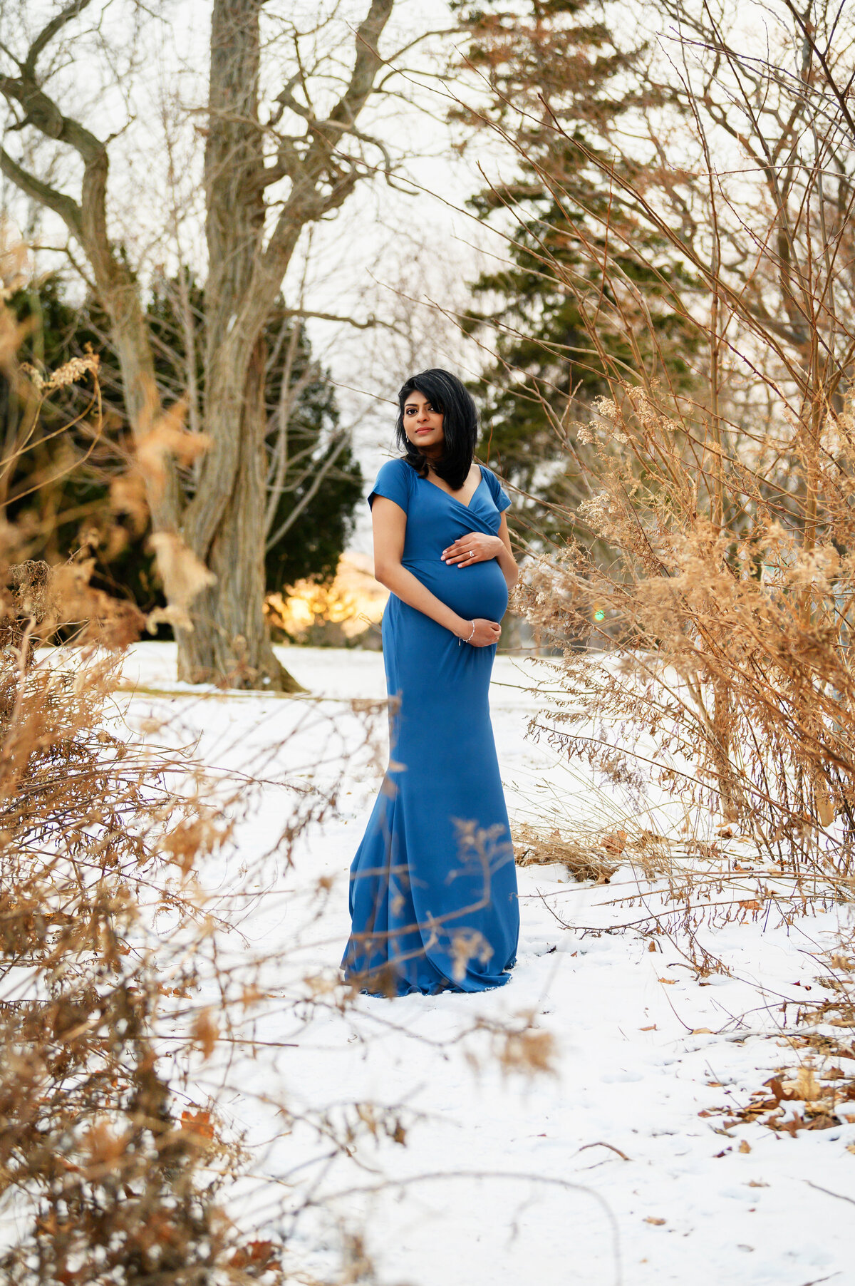 Pregnant woman wearing a blue maternity dress outdoors in the snow for her Burlington, ON maternity photos