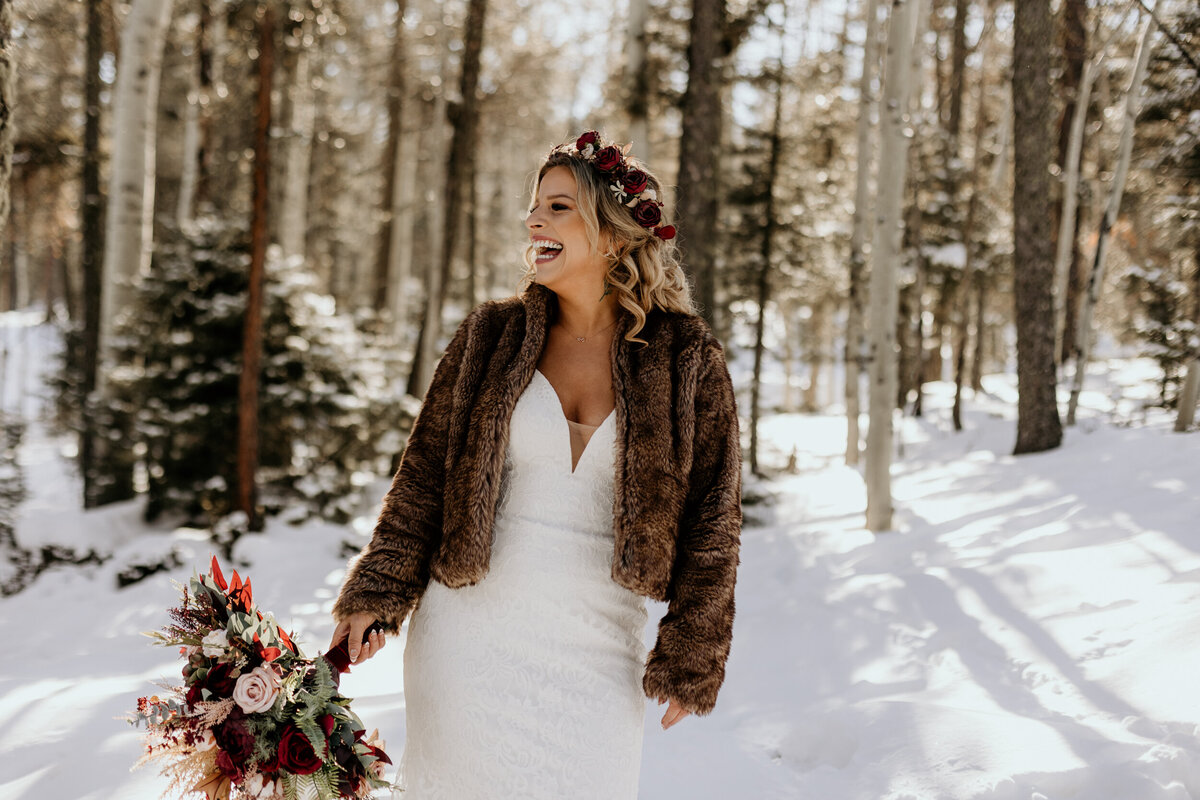 bride standing in a snowy forest laughing